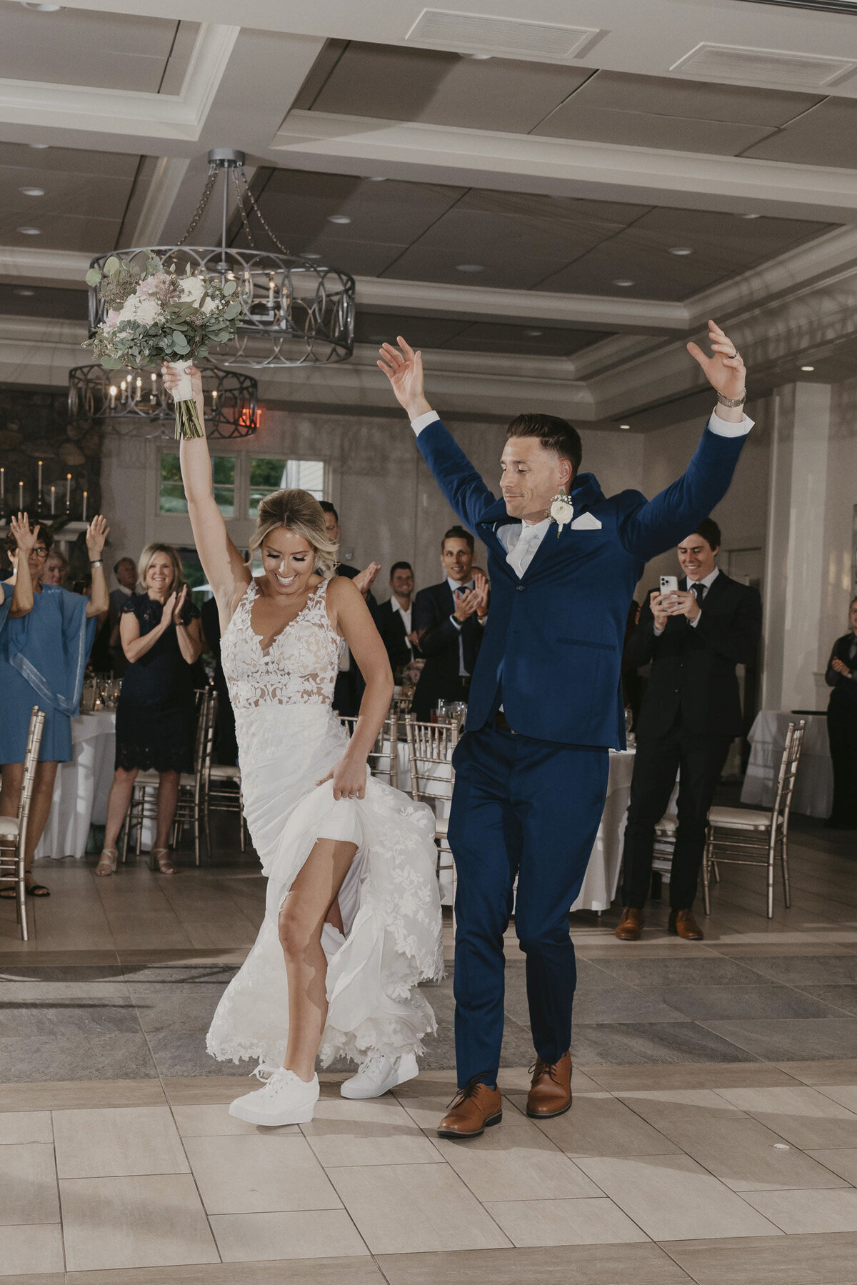 Bride with white tennis shoes and groom celebrating in a reception hall