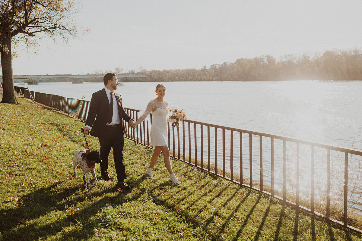 Bride and Groom hold hands and walk dog in front of The Kennedy Center in Washington DC