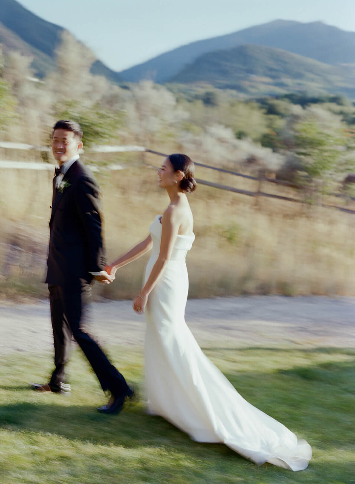 Bride and groom in motion pose for pictures after their Aspen Meadows Resort wedding ceremony taking place outdoors among beautiful scenery.