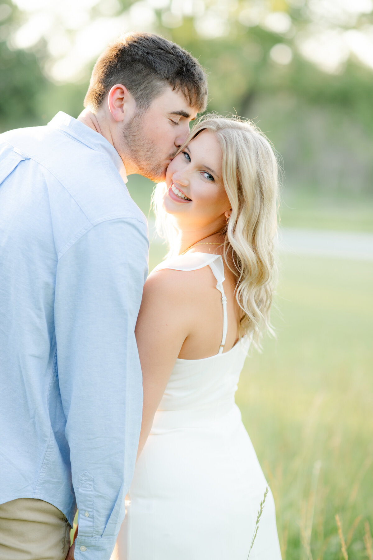 man kisses girls cheek standing in tall grass field