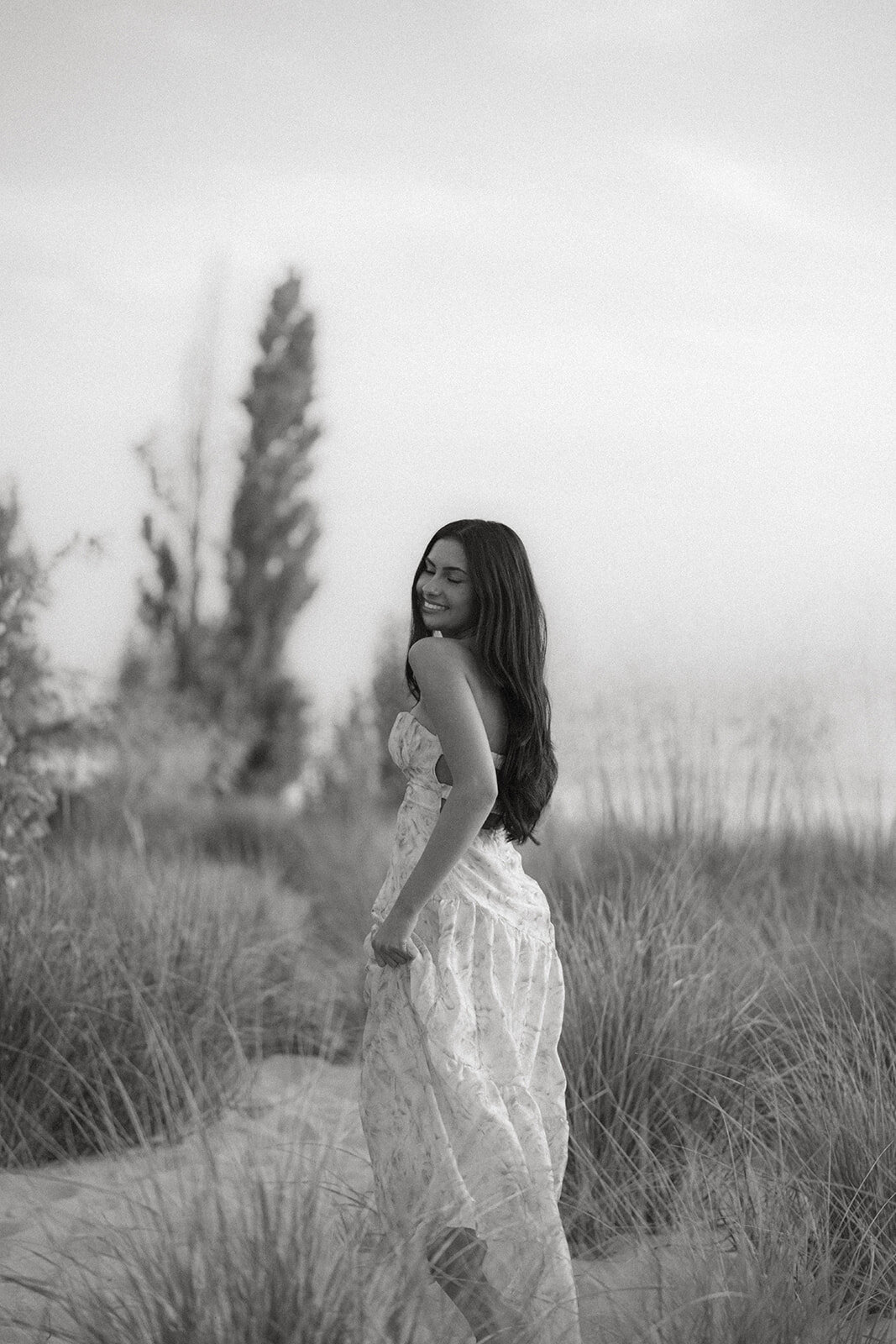 Black and white photo of a high school senior standing in the dunes at South Haven North Beach during her senior pictures.
