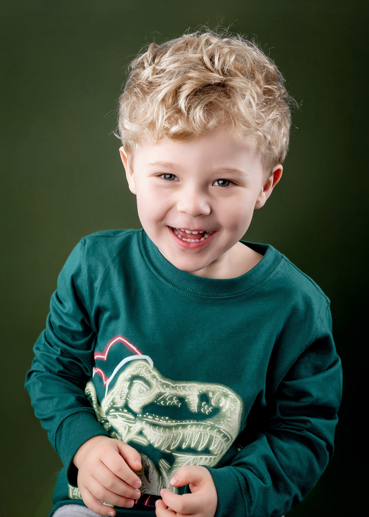A boy with curly, blond hair smiles on a green background