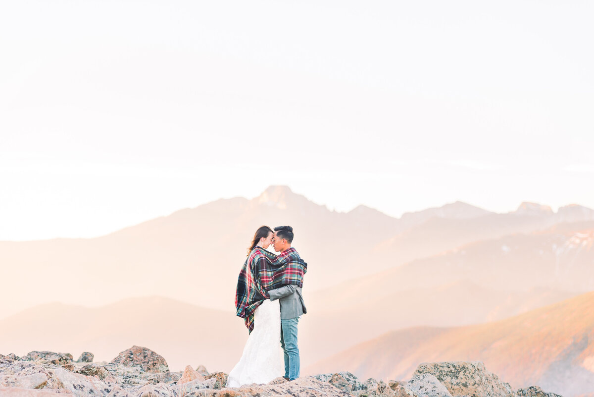 epic colroado location in rocky  mountain national park  for bride and groom photos at sunrise as the couple touches foreheads and shares an embrace at sunrise with pink and purple mountains in the background  in estes park by colorado wedding photographer kari joy photography