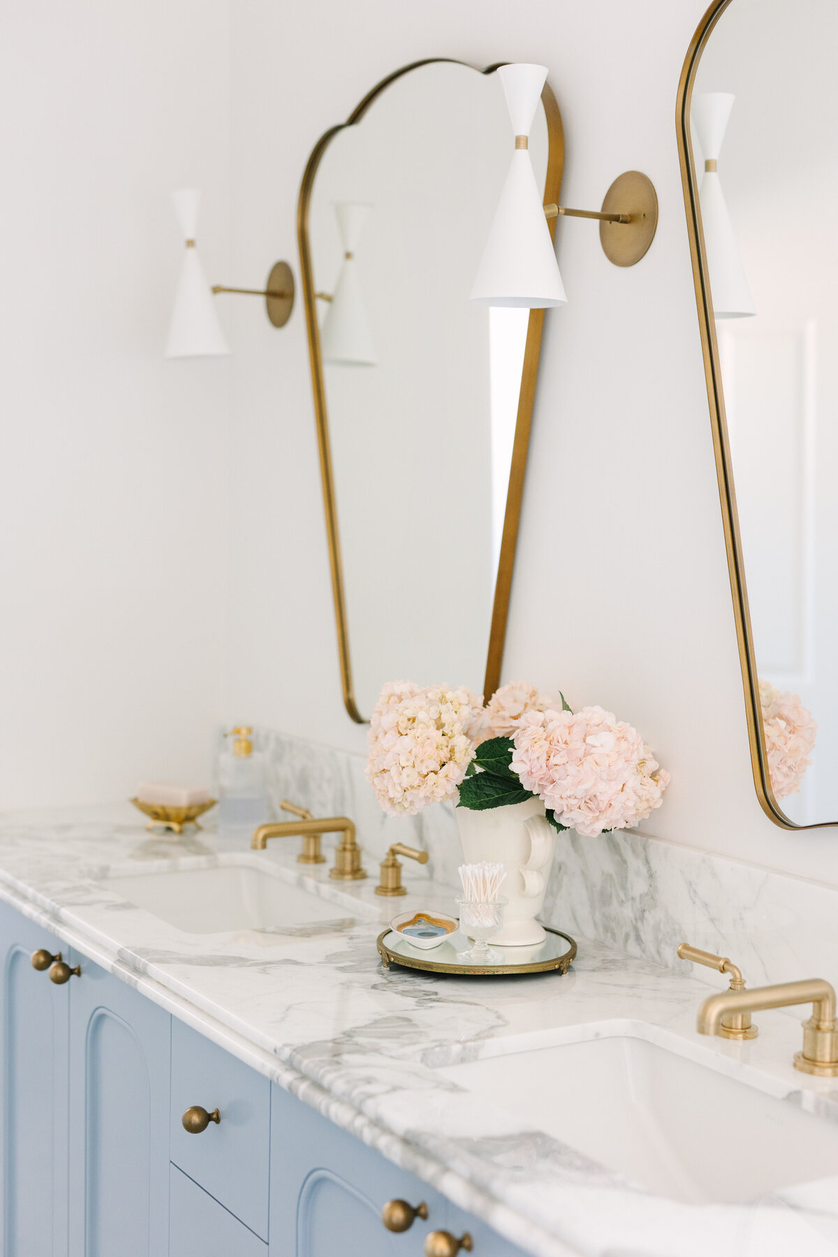 Primary bathroom with a custom vanity in Sherwin Williams Lakeside and rounded edges, Arabescato Corchia marble counters, Italian shield mirrors, and Blueprint Lighting Monolith Wall Sconce. 