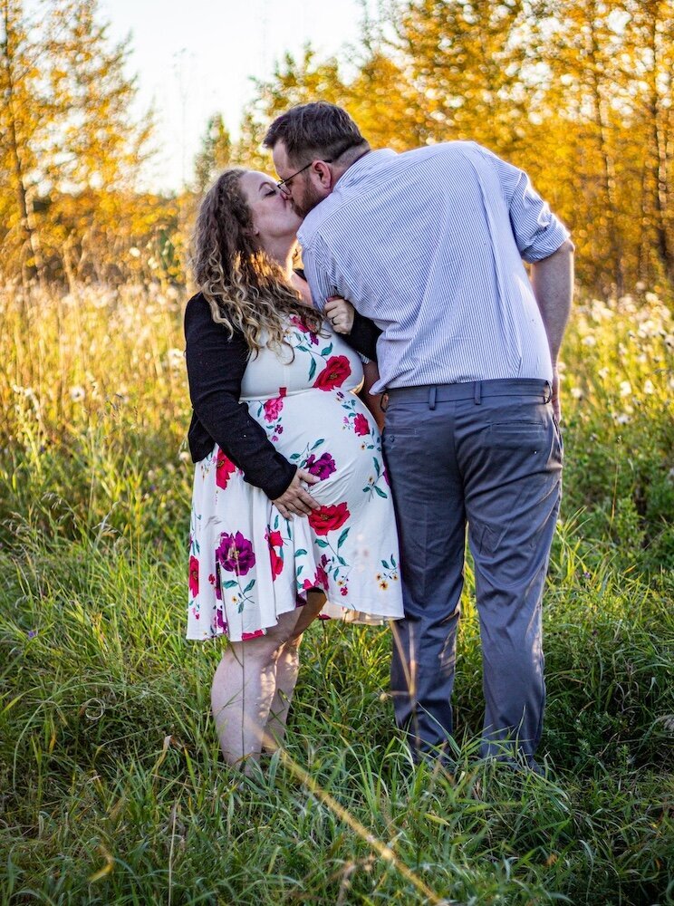 a pregnant woman holding her belly is kissing her husband