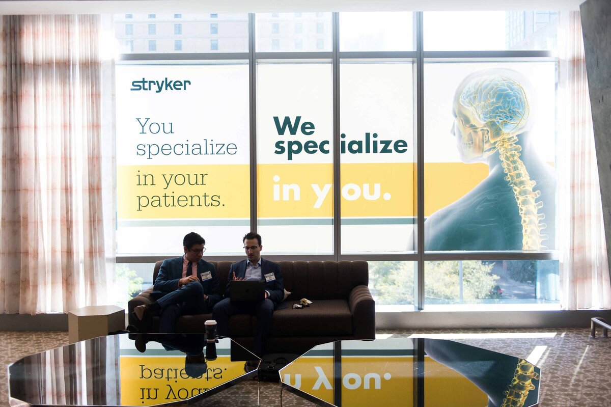 Two attendees sit in front of Stryker window cling illuminated behind them