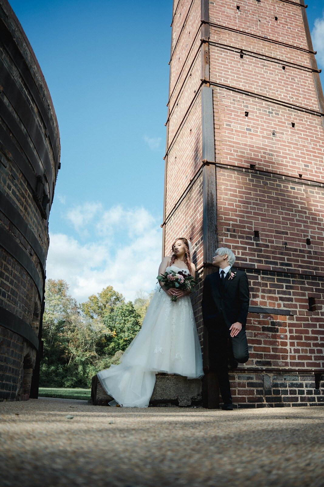 Groom leaning on a brick wall while watching her bride