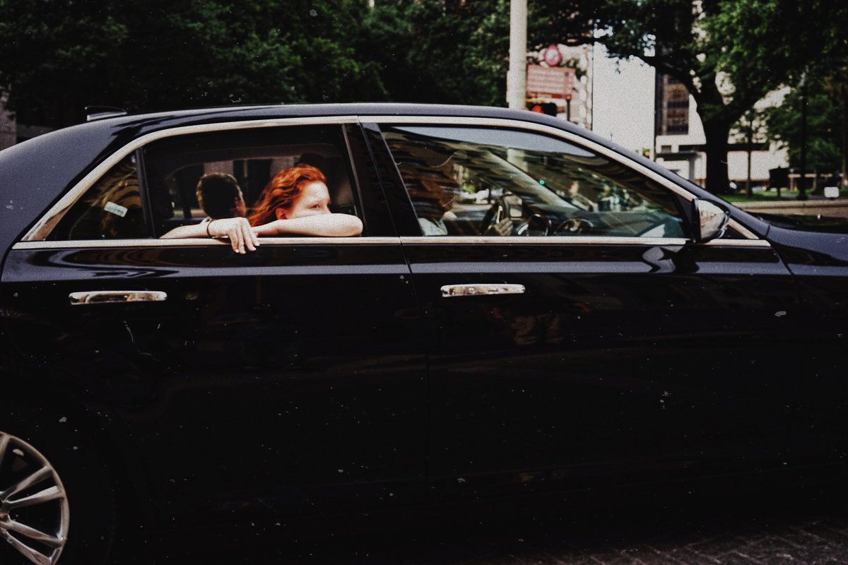 Redhead riding in the backseat of a black car with the windows down