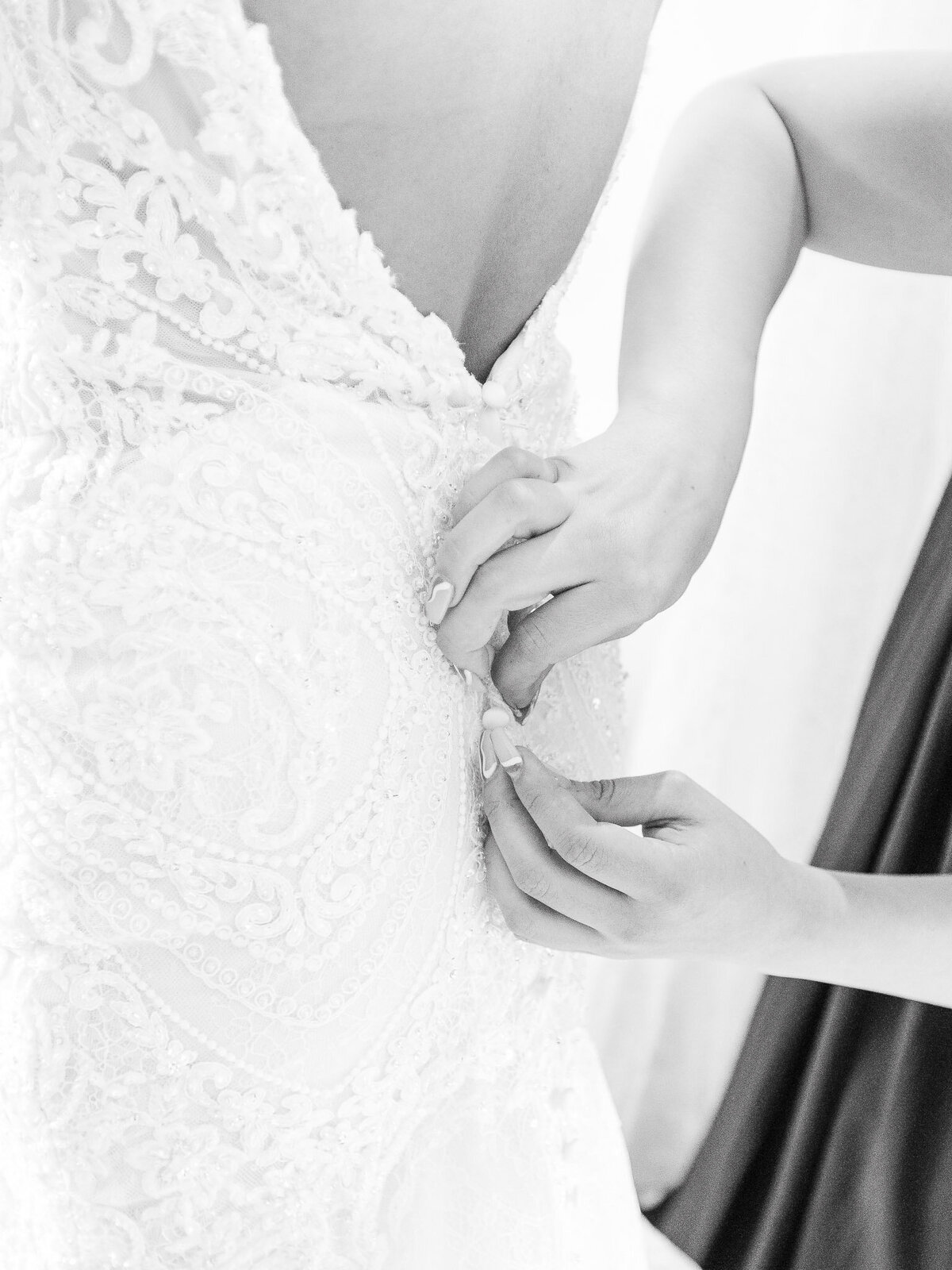 Close-up of a bridesmaid fastening the delicate buttons on a bride’s lace wedding dress at the Ritz-Carlton Laguna Niguel