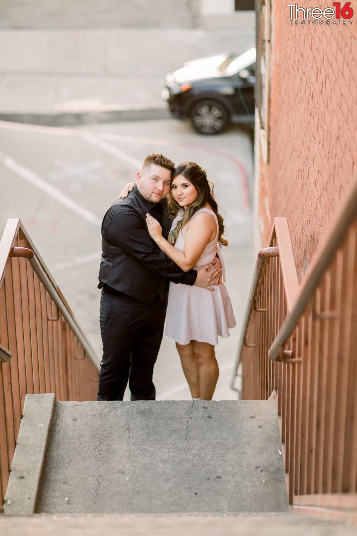 Engaged couple embrace while standing on an outdoor stairwell