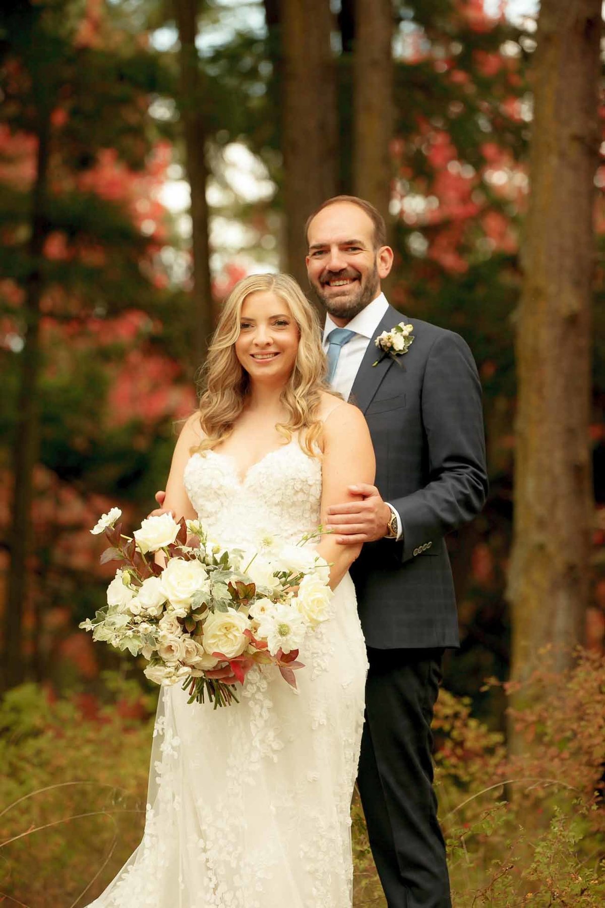 bride and groom in forest with bouquet of white and ivory fall flowers