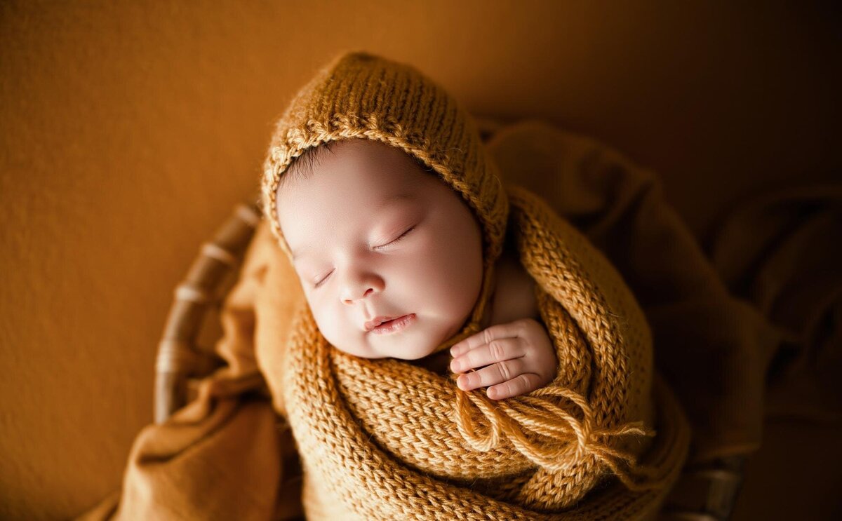 Baby with his mouth open laying on a knitted light brown blanket