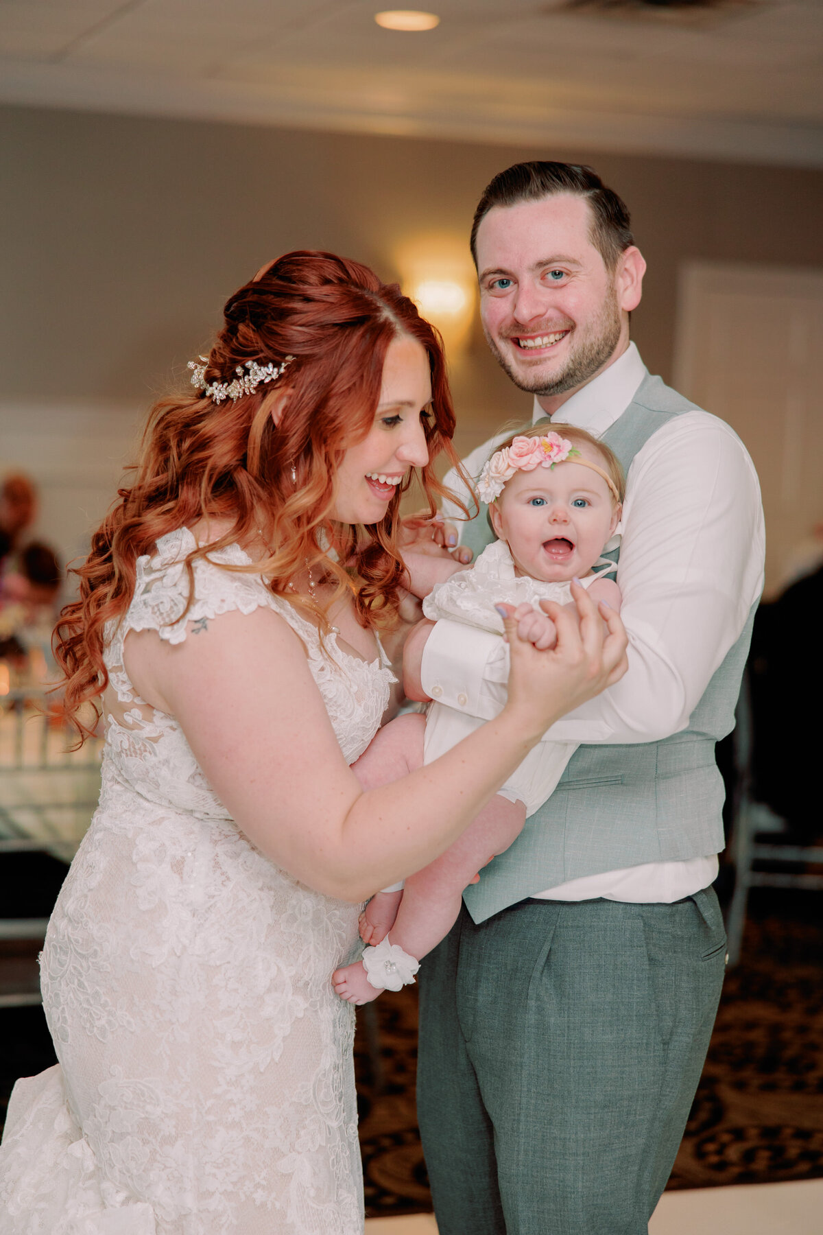 A newlywed couple smiling as one holds a baby in their arms 