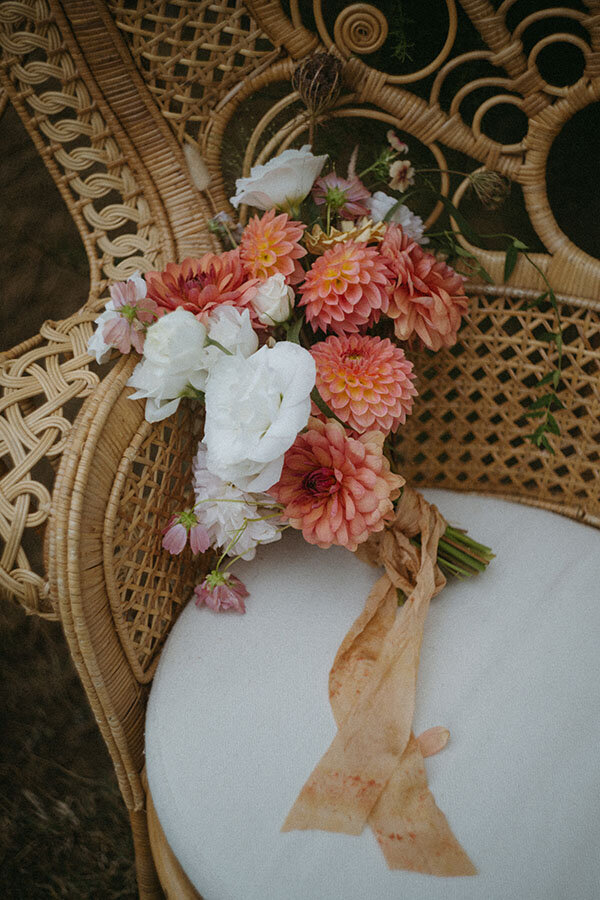 Bouquet de fleurs pastel posé sur un fauteuil en rotin. Détail bohème capturé par Kamescop lors d'un mariage à Saint-Quay-Portrieux.