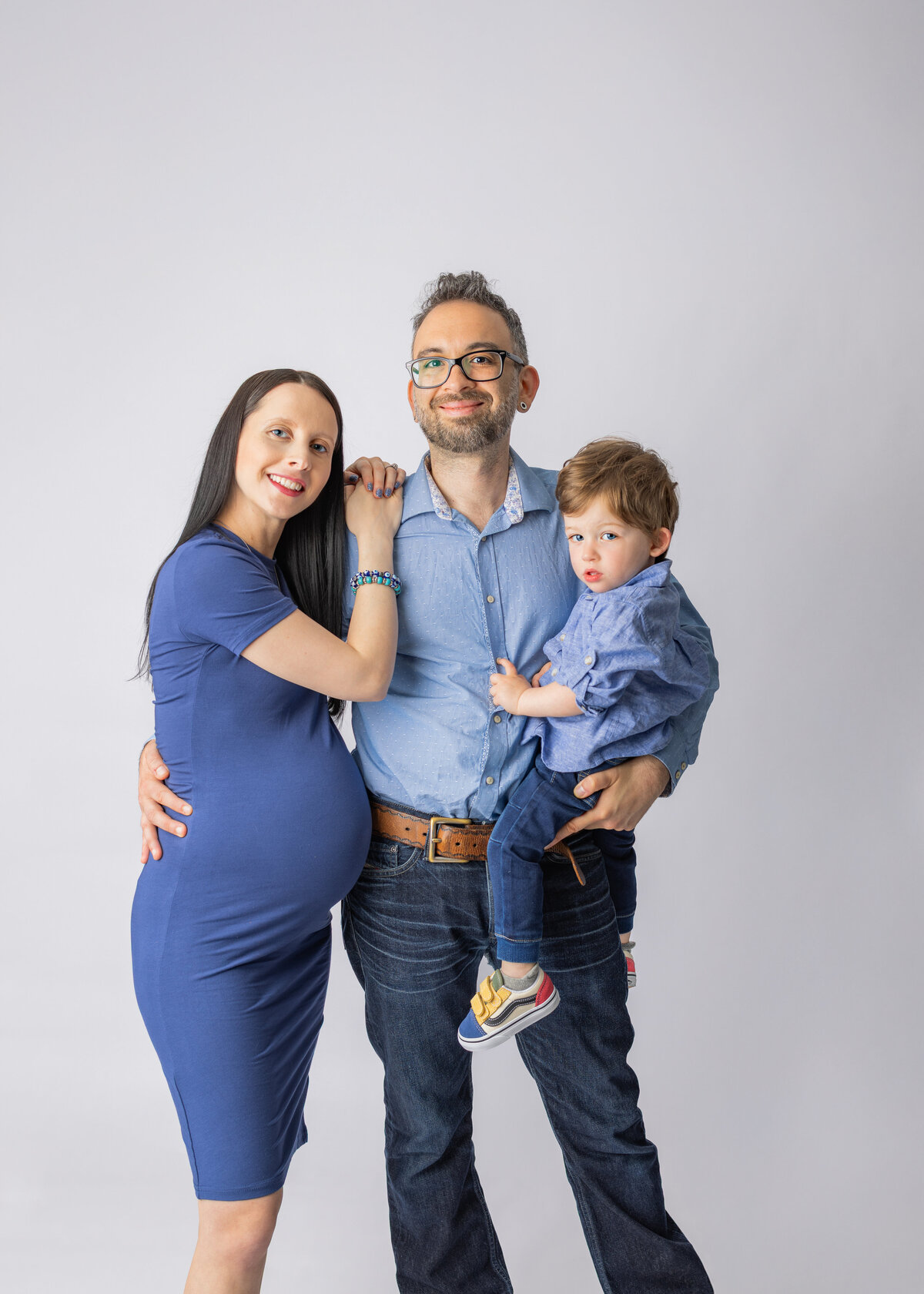 Expecting parents smiling with young son during family maternity photoshoot in Bergen County New Jersey studio"