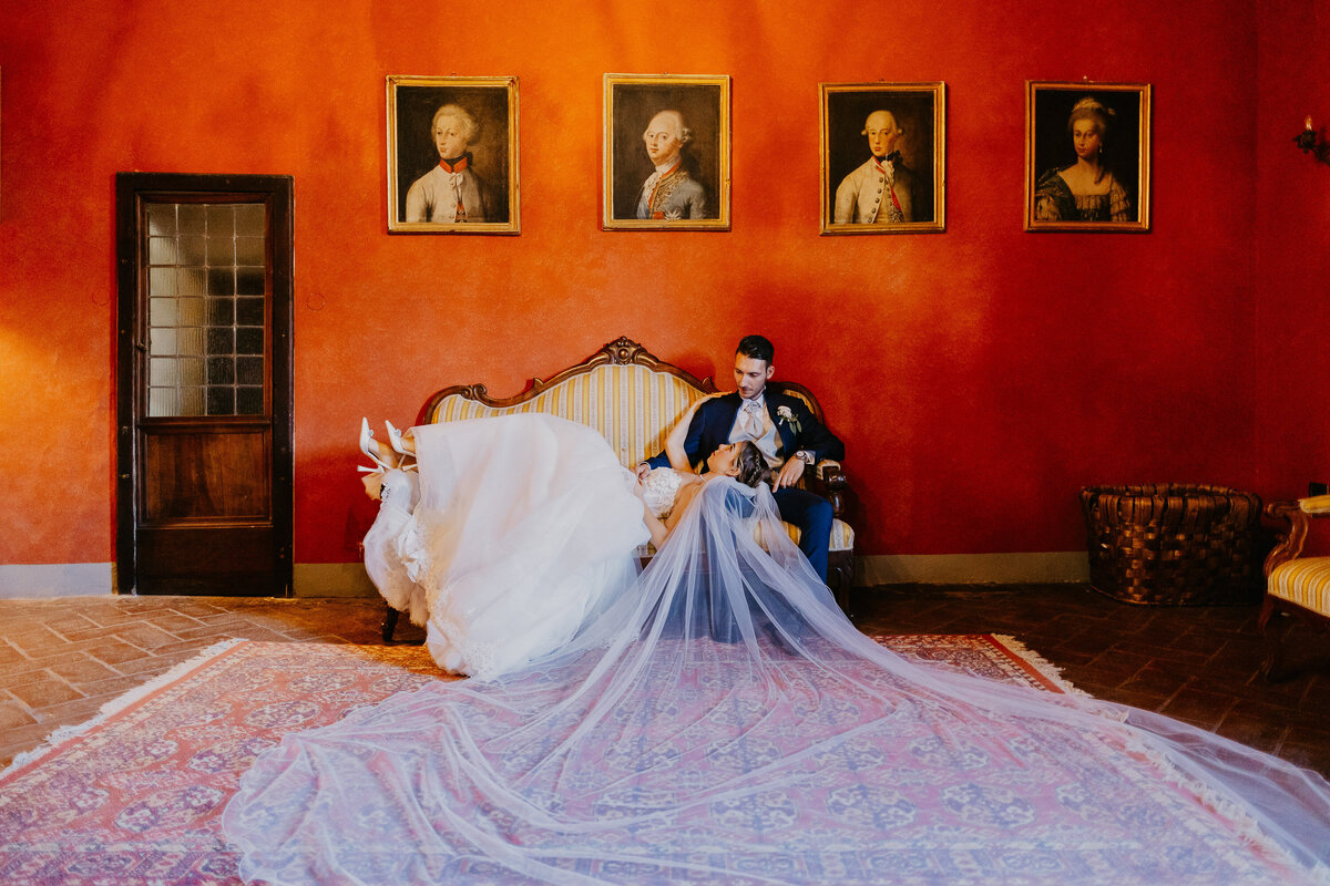 Bride and groom seated on historic sofa with long veil, Castello il Palagio wedding photographer Tuscany.