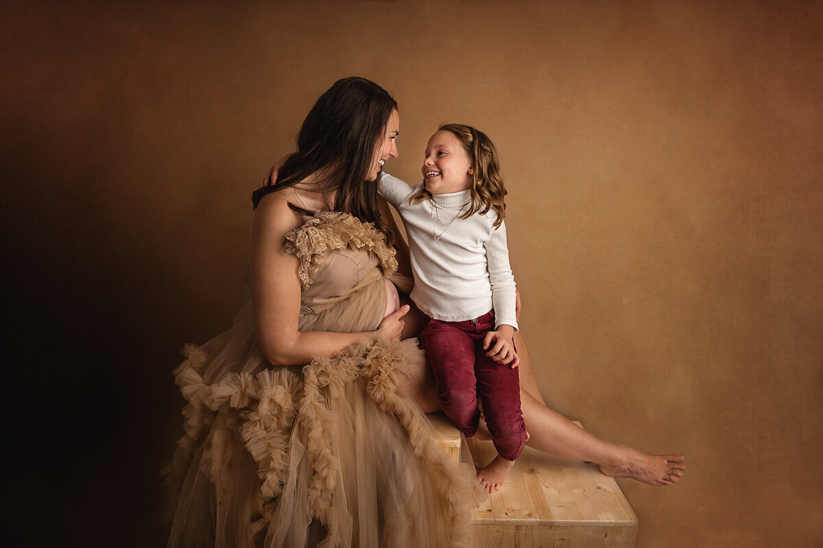 Young girl hugging her mom expectant of a baby, smiling at each other.