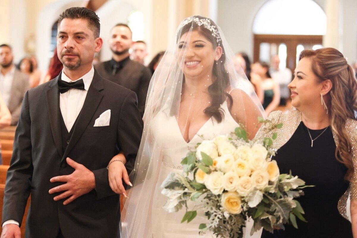 Bride walks down the aisle holding bouquet with parents on either side at Union Club Hotel.