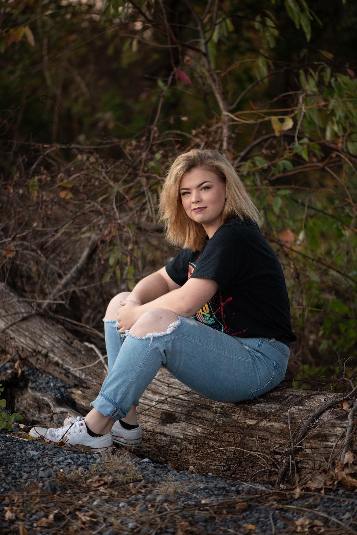 Senior girl in torn jeans seated on log