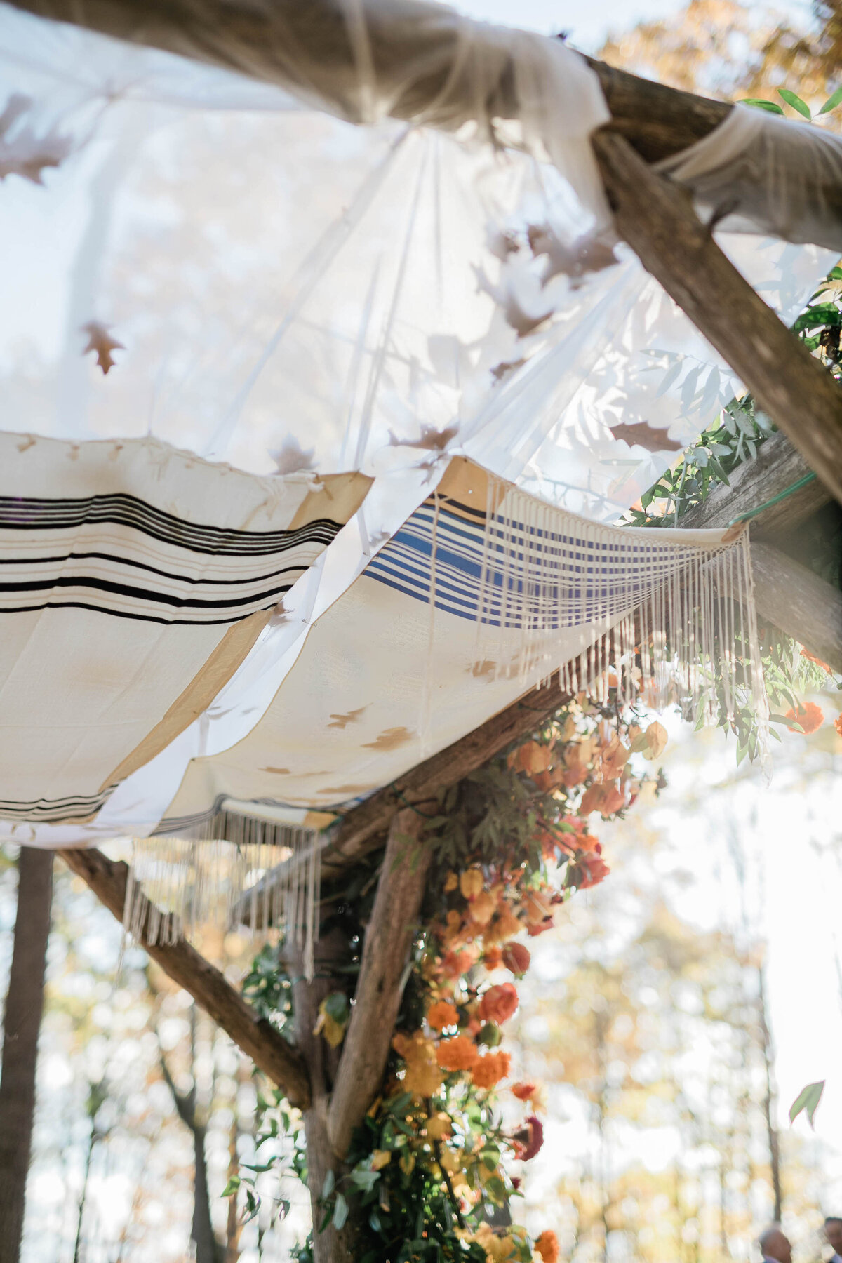 A close-up of the chuppah canopy, featuring a traditional tallit with blue and black stripes and delicate fringe