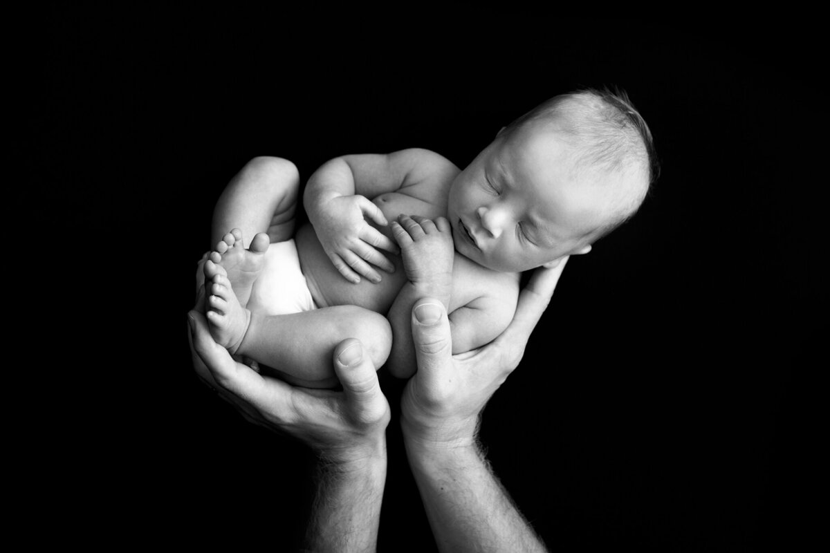 nyfödd bebis hålls i pappans händer i svartvitt