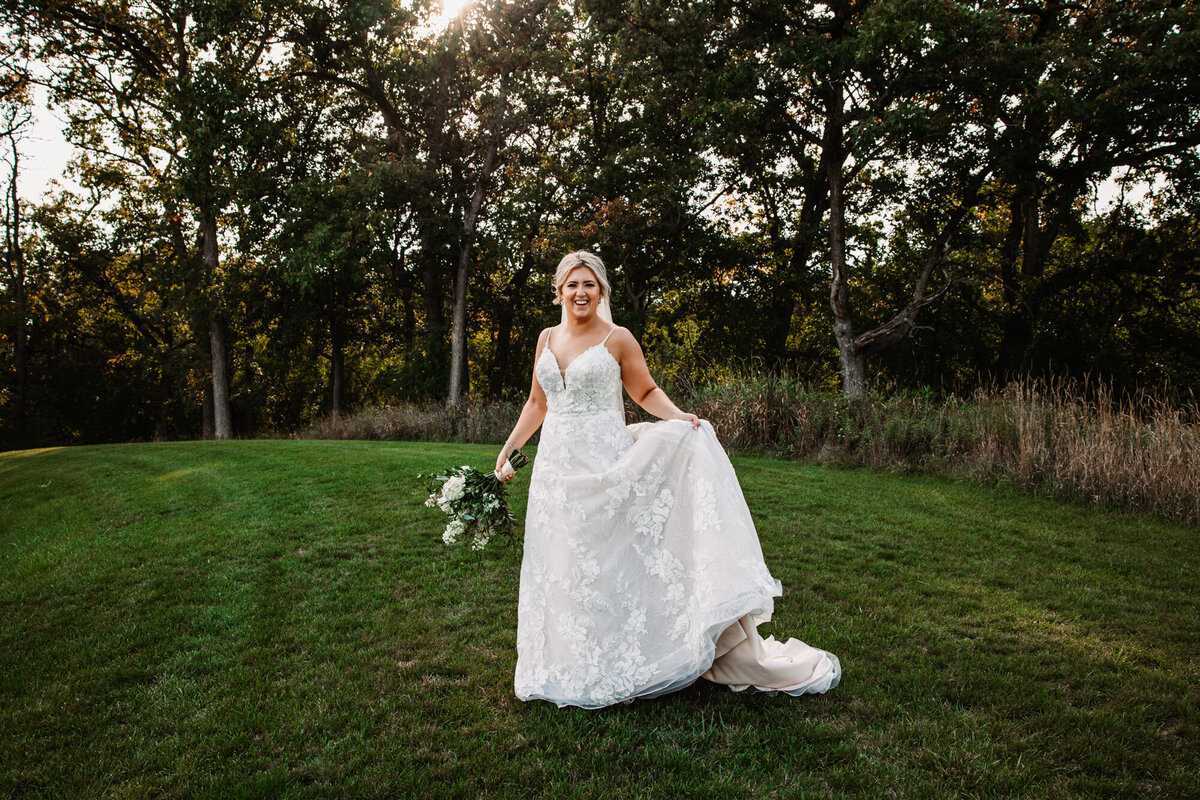 bride holds dress to twirl in grass