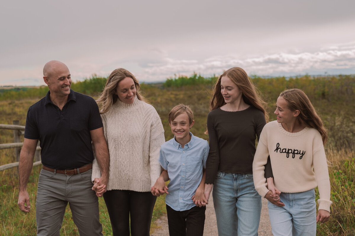 Family walking in open meadow in Cochrane with Rocky Mountain views behind.