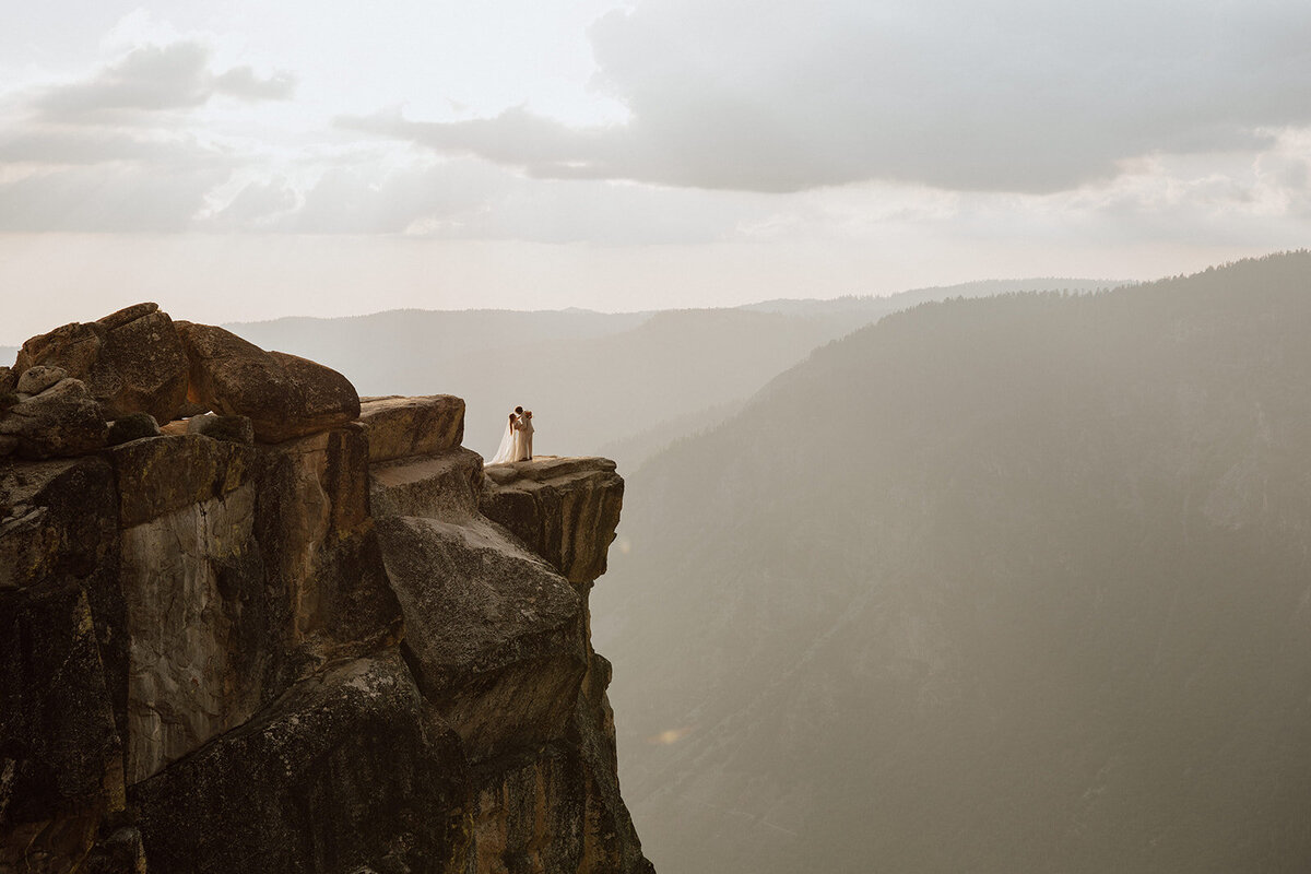 couple standing on a rocky cliff overlooking yosemite valley