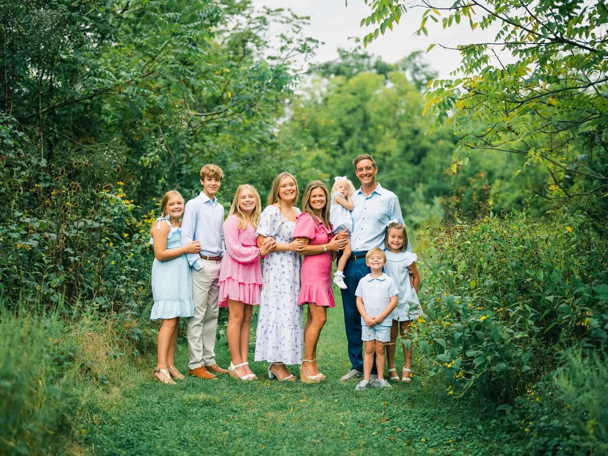 Parents with a large family smiling and standing on a grassy path.