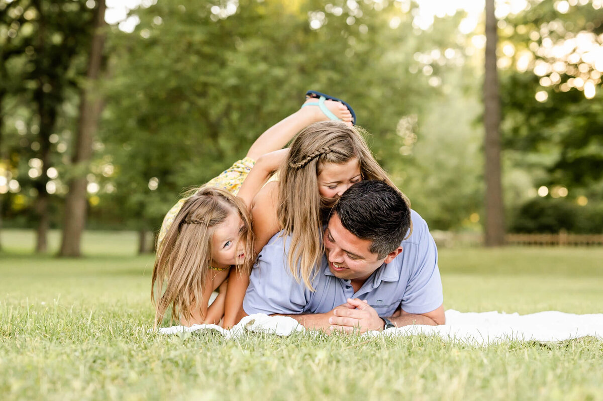 Energetic Girls crawling on top of dad during family session at Fabyan Forest Preserve in Geneva.