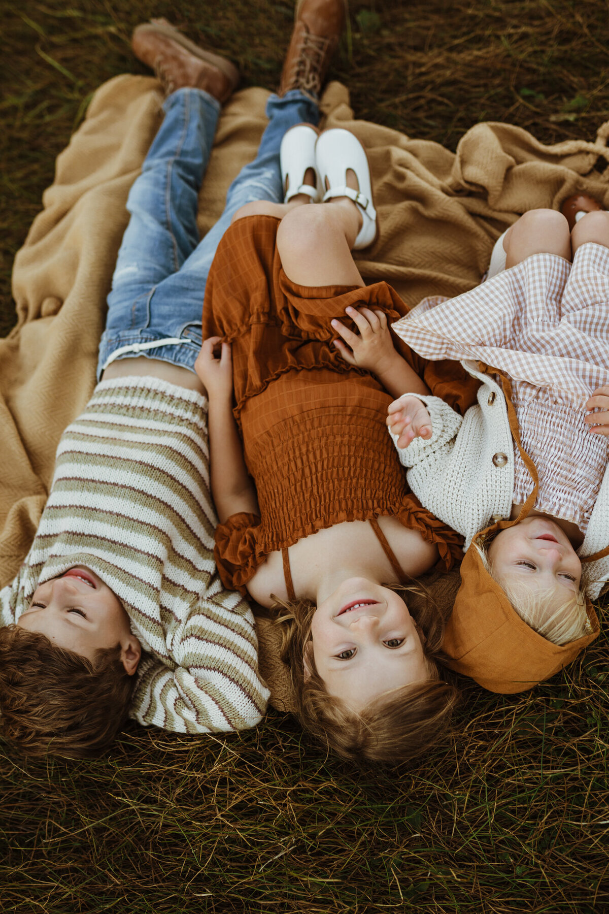 Three young siblings are all laying down on the ground in a line next to each other as the camera points down at them