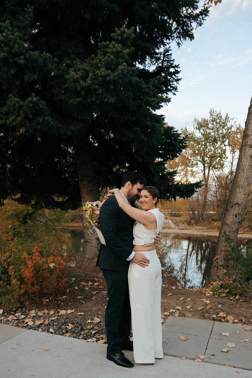 A couple embrace and smile while standing near a body of water in Boise.