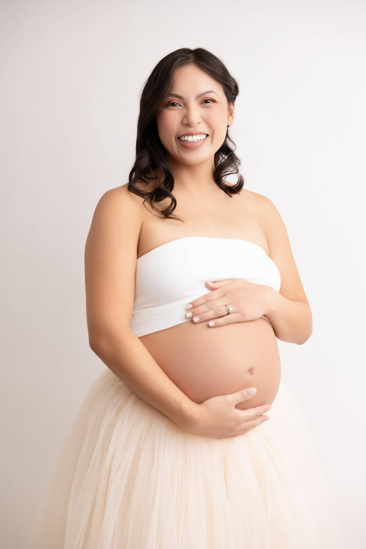 close-up image of pregnant mom wearing white tube top and light pink skirt.