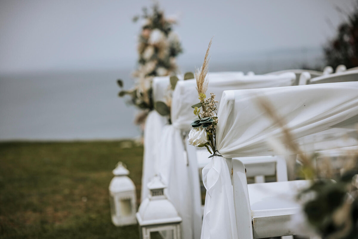 A row of white chairs sitting next to each other with flowers and chair sashes