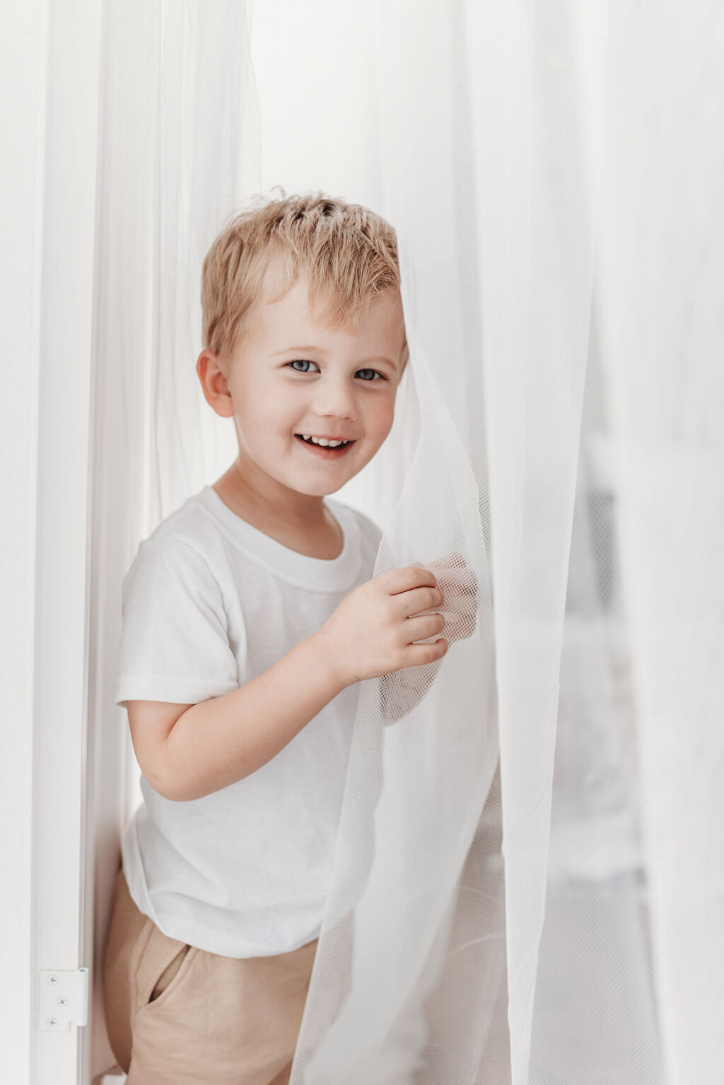 little boy in the curtains of Denver milestone photographer Alyssum Hutchison's studio