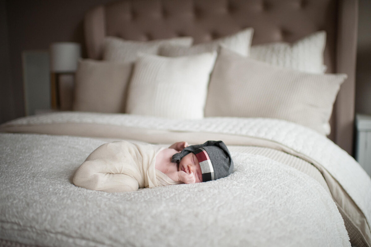 A newborn baby sleeps on a bed in a white onesie and grey sleep cap