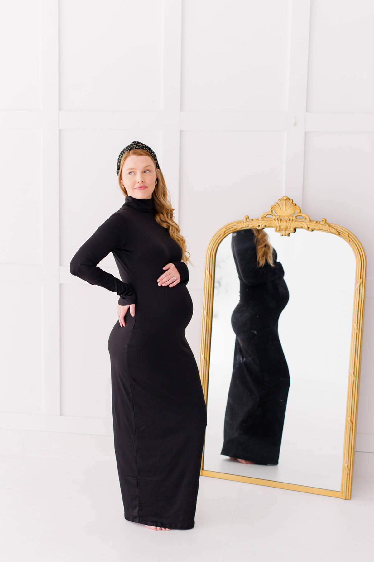 Pregnant mother stands near mirror showing her bump while also smiling off in the distance