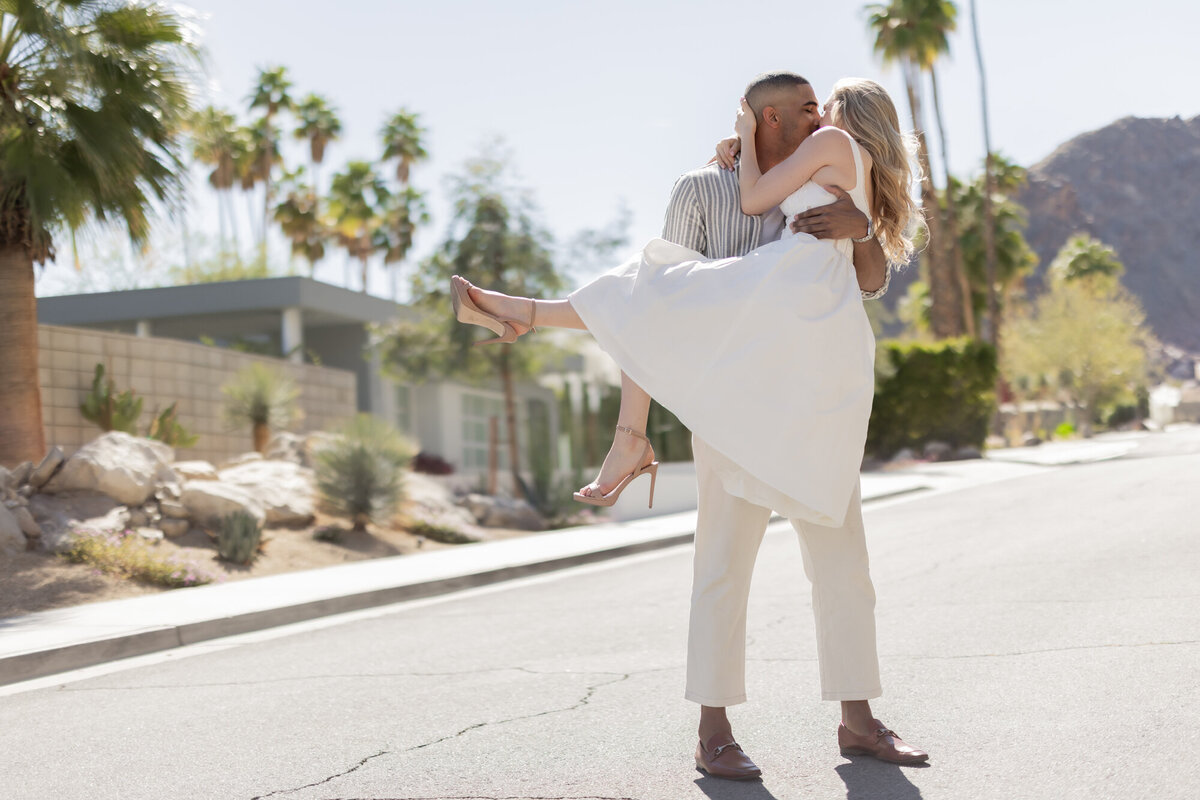 Couple walking through a sunlit street, hand in hand, sharing a carefree moment with Palm Springs palms behind them.