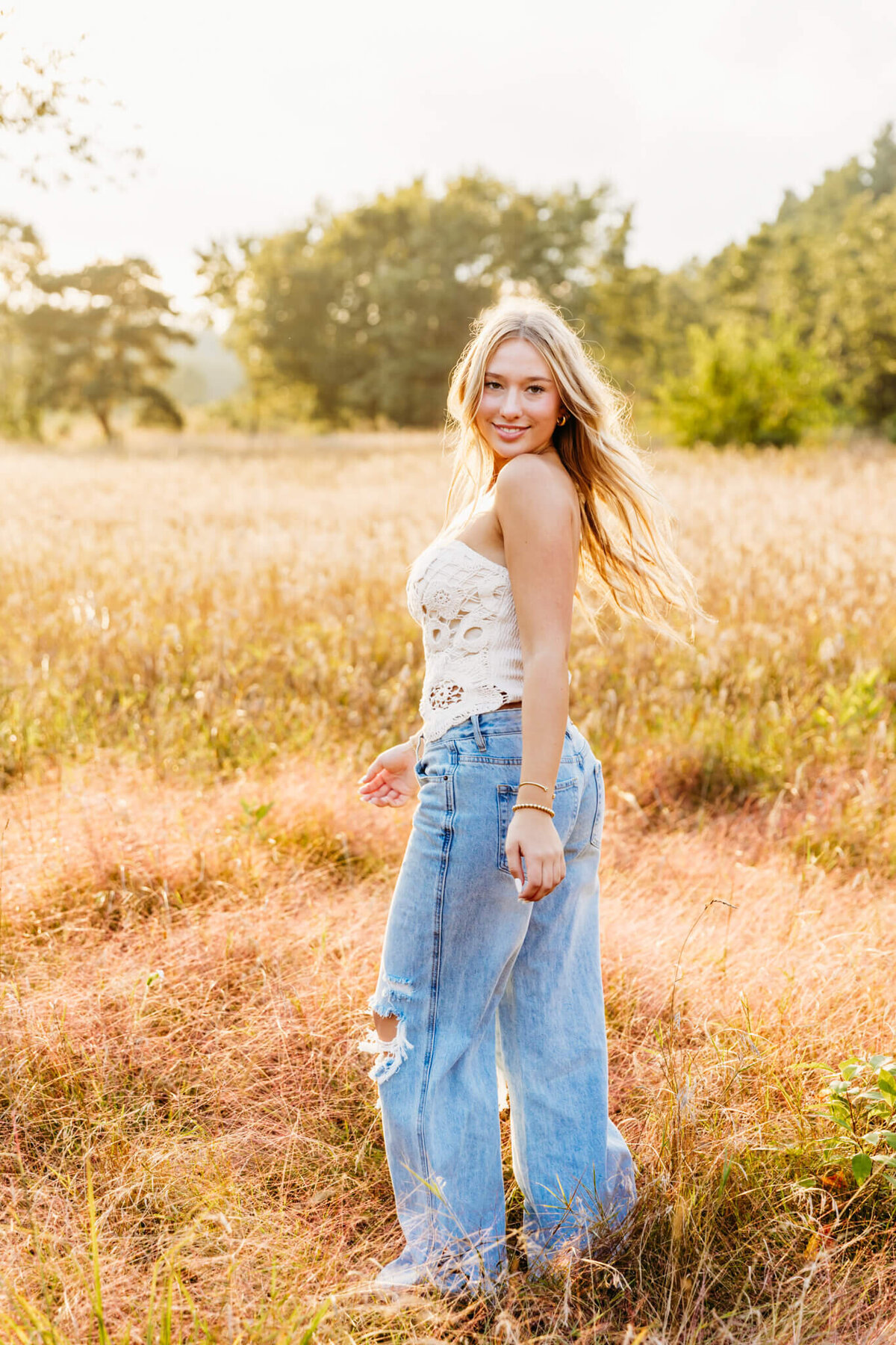 gorgeous blonde teenage girl in a lace top and jeans spinning and looking back as she walks in a glowing field