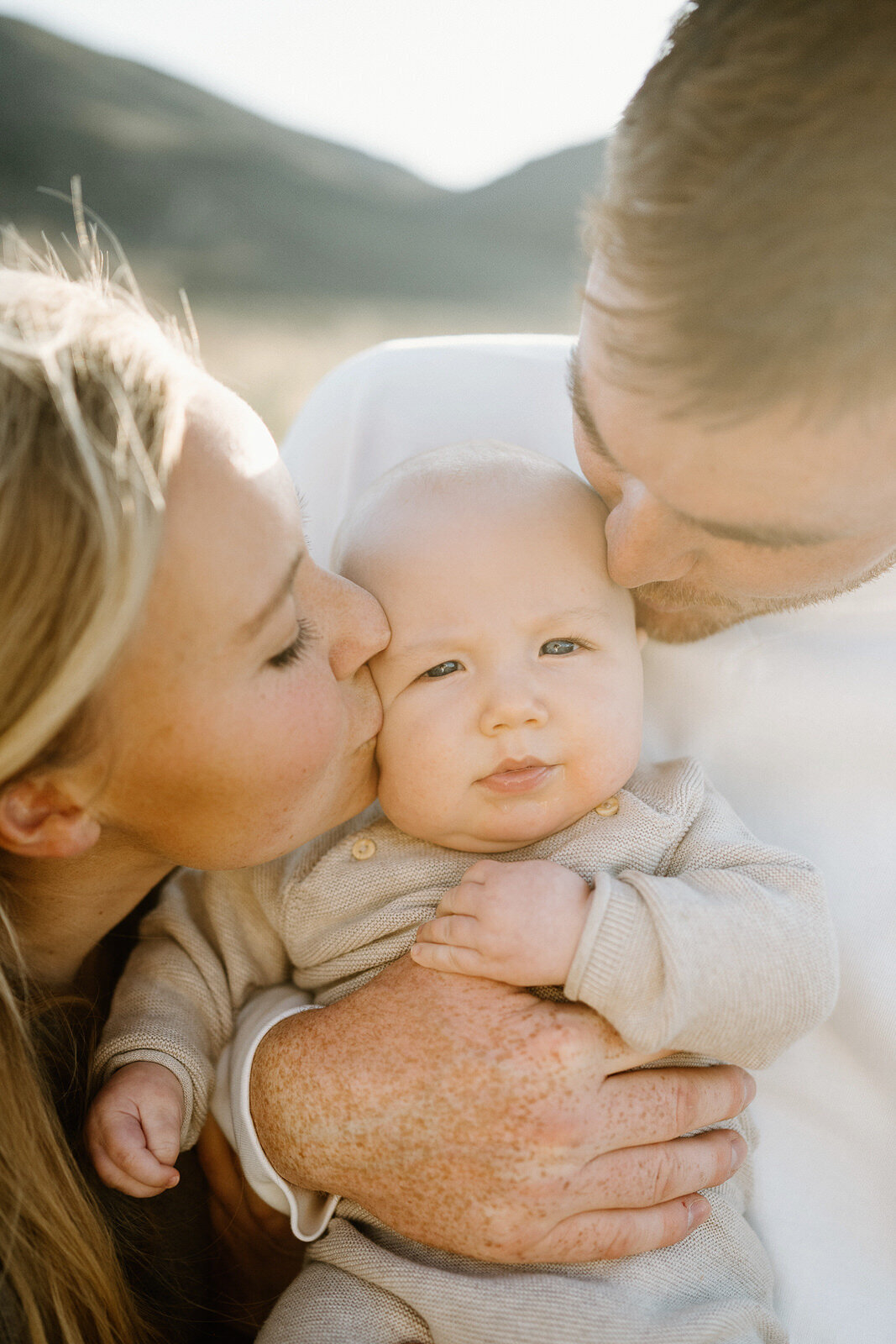 Parents kiss baby in mountain glow