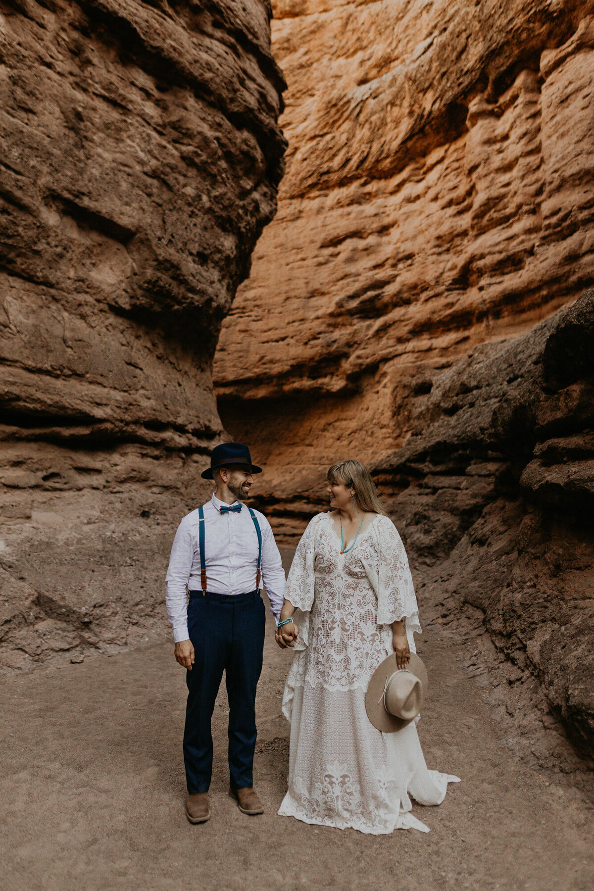 bride and groom standing in a slot canyone holding hands