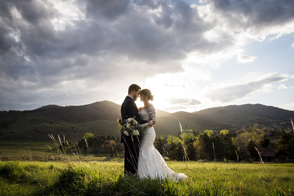 A bride and groom stand forehead to forehead with the mountains in the background.