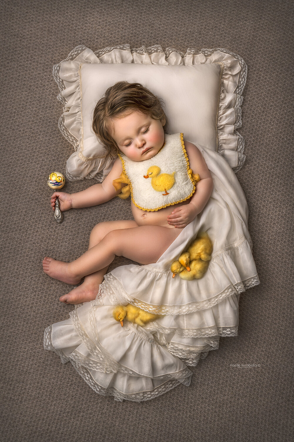 Baby wearing ducky bib sleeping with vintage blankets and baby ducklings.