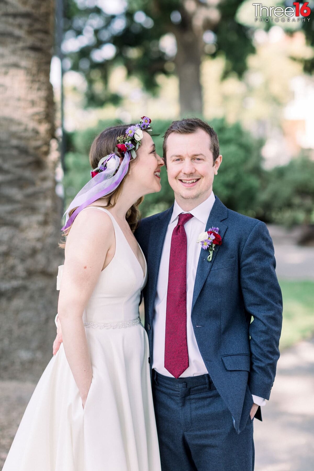 Groom smiles as his Bride whispers into his ear