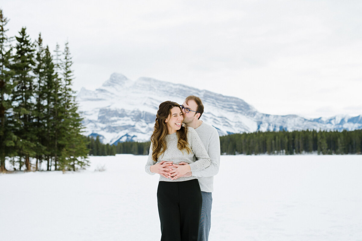 Adorable couple embracing  during their snowy engagement session, in the mountains, captured by Christy D. Swanberg Photography, editorial elopement and wedding photographer in Calgary, Alberta, featured on the Bronte Bride Vendor Guide.