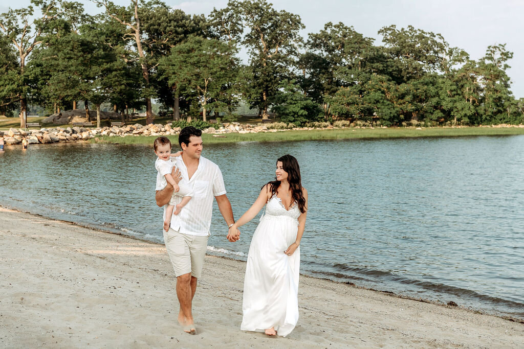 Connecticut maternity photographer documents expecting family walking hand in hand along coastal beach