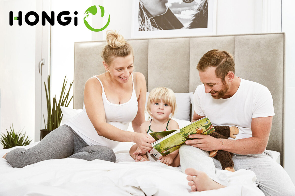 Authentisches Familienbild in heller Schlafzimmeratmosphäre – Werbeshooting für HONGi Matratzen, fotografiert von Atelier Schulte. Emotionale Lifestylefotografie für Markenkommunikation.