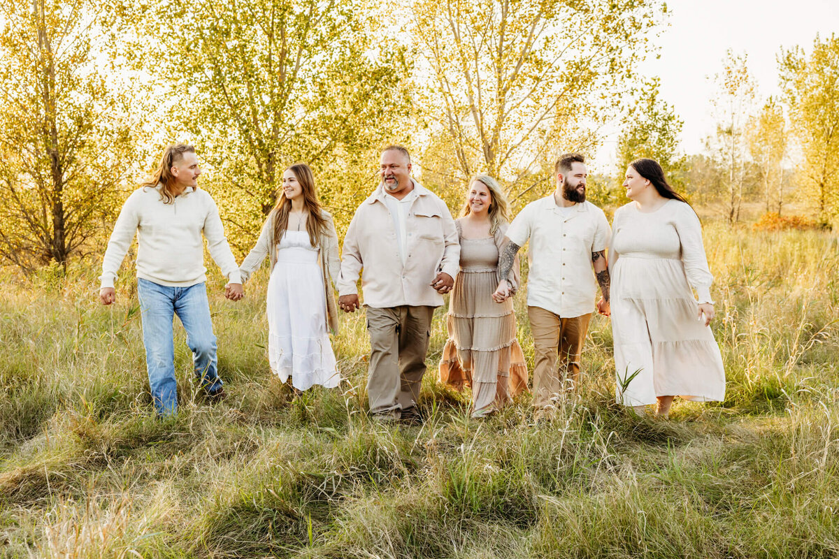 family dressed in various cream colors walking through a fall colored field captured by Milwaukee family photographer Ashley Kalbus