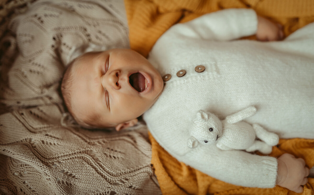 Baby with his mouth open laying on a knitted light brown blanket