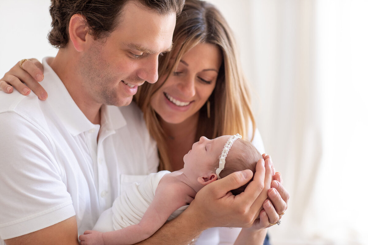 A father gently holds a newborn baby while both parents gaze at their child with loving smiles, sharing a tender and joyful moment.